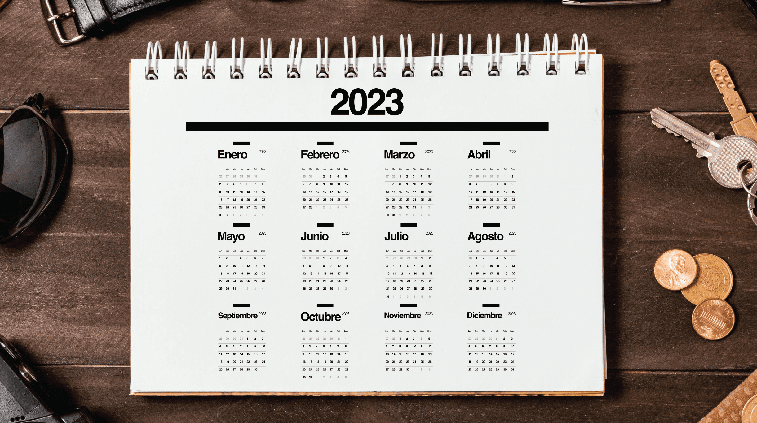 "Premium custom printed spiral desk calendar displaying a full 12-month grid overview template on a rich dark wooden table background surrounded by office keys and coins."
